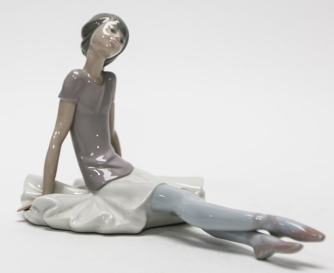 Lladró Resting Ballerina Porcelain Figurine: Graceful Lladró porcelain figurine depicting a seated ballerina resting after her performance, with extended legs, pale blue tights, lavender slippers, and a flowing white tutu. Finished in Lladró��