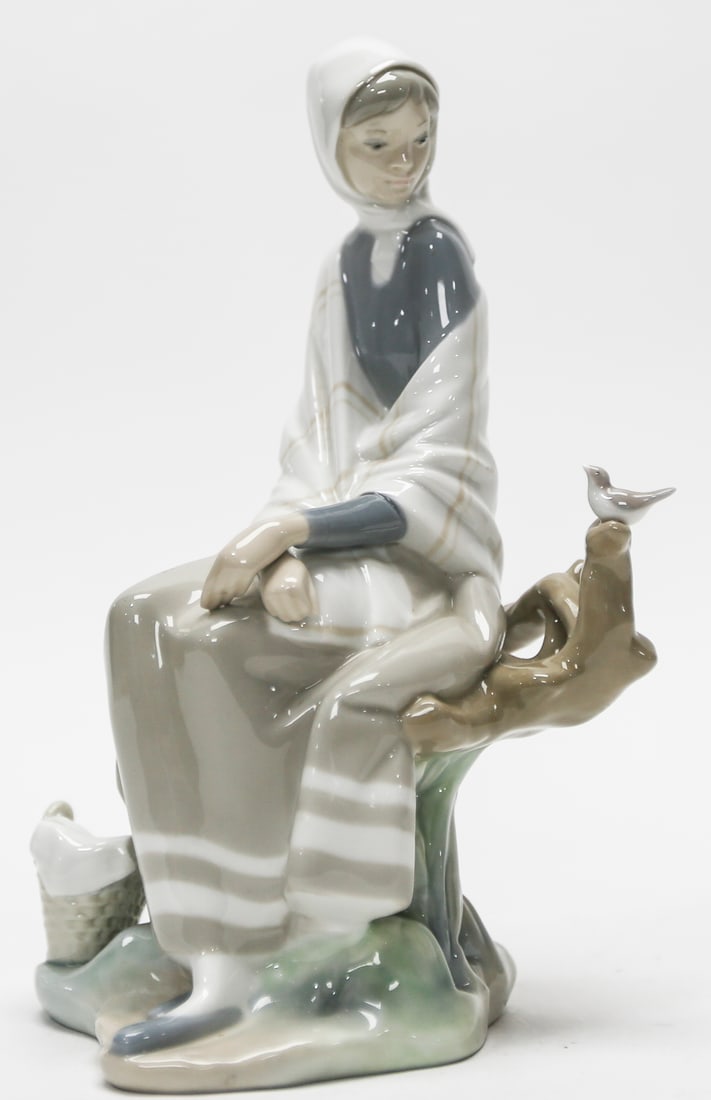 Lladró Shepherdess with Bird Figurine: Glossy Lladró porcelain figurine depicting a seated shepherdess wrapped in a softly striped shawl, with a small bird perched on a sculpted tree branch and a basket resting beside her. Finished in