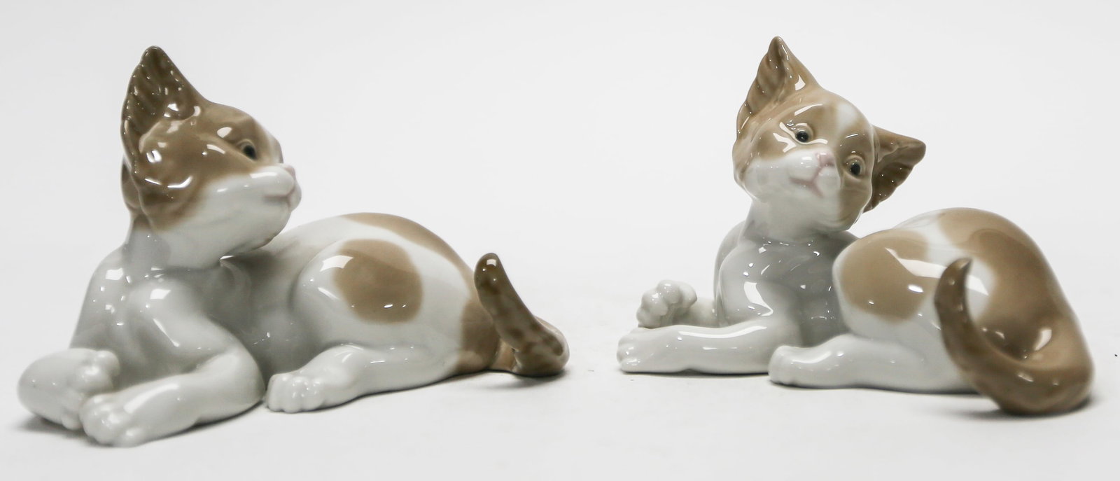 Lot of Two Lladro Playful Cat Porcelain Figurines No. 5091: A lot of two matching retired Lladro glazed porcelain figurines titled Playful Cat, model No. 5091, each depicting a reclining brown and white kitten with curled tail and raised head. Handmade in