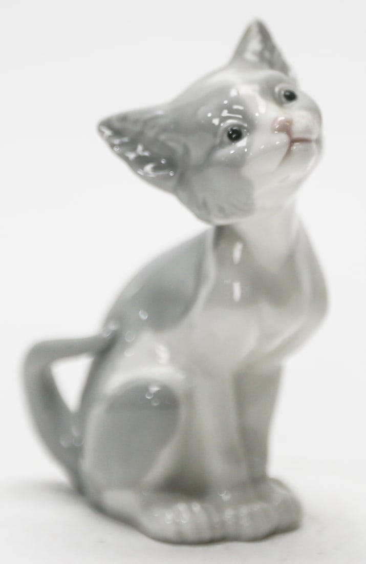 Lladro Feed Me Cat Porcelain Figurine No. 5113: A retired Lladro glazed porcelain figurine titled Feed Me, model No. 5113, depicting a seated gray and white kitten looking upward with its tail curled around its body. Designed by Salvador Debon and
