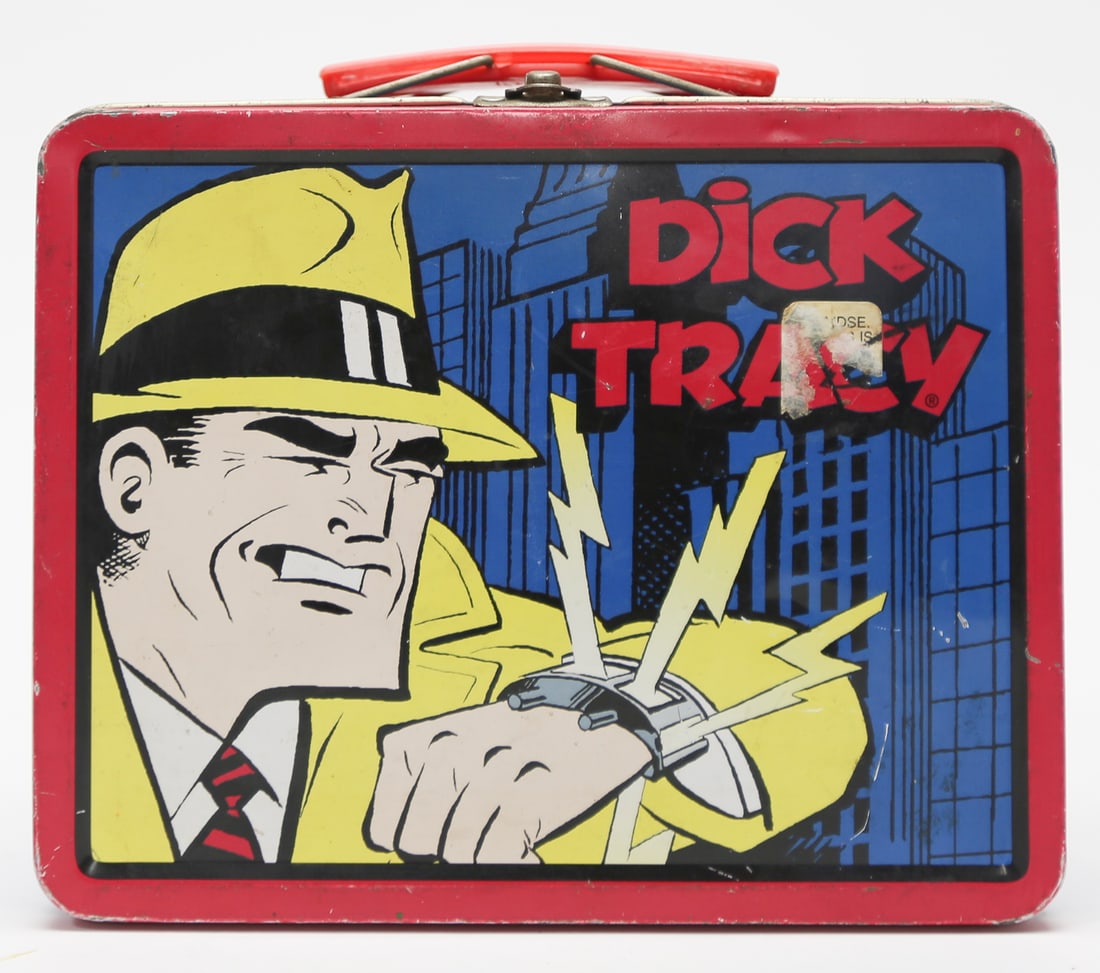 Dick Tracy Metal Lunch Box: A metal lunch box featuring comic-strip detective Dick Tracy in his signature yellow fedora and coat, shown using his wrist radio against a blue cityscape. The box has red and blue enameled panels, a 