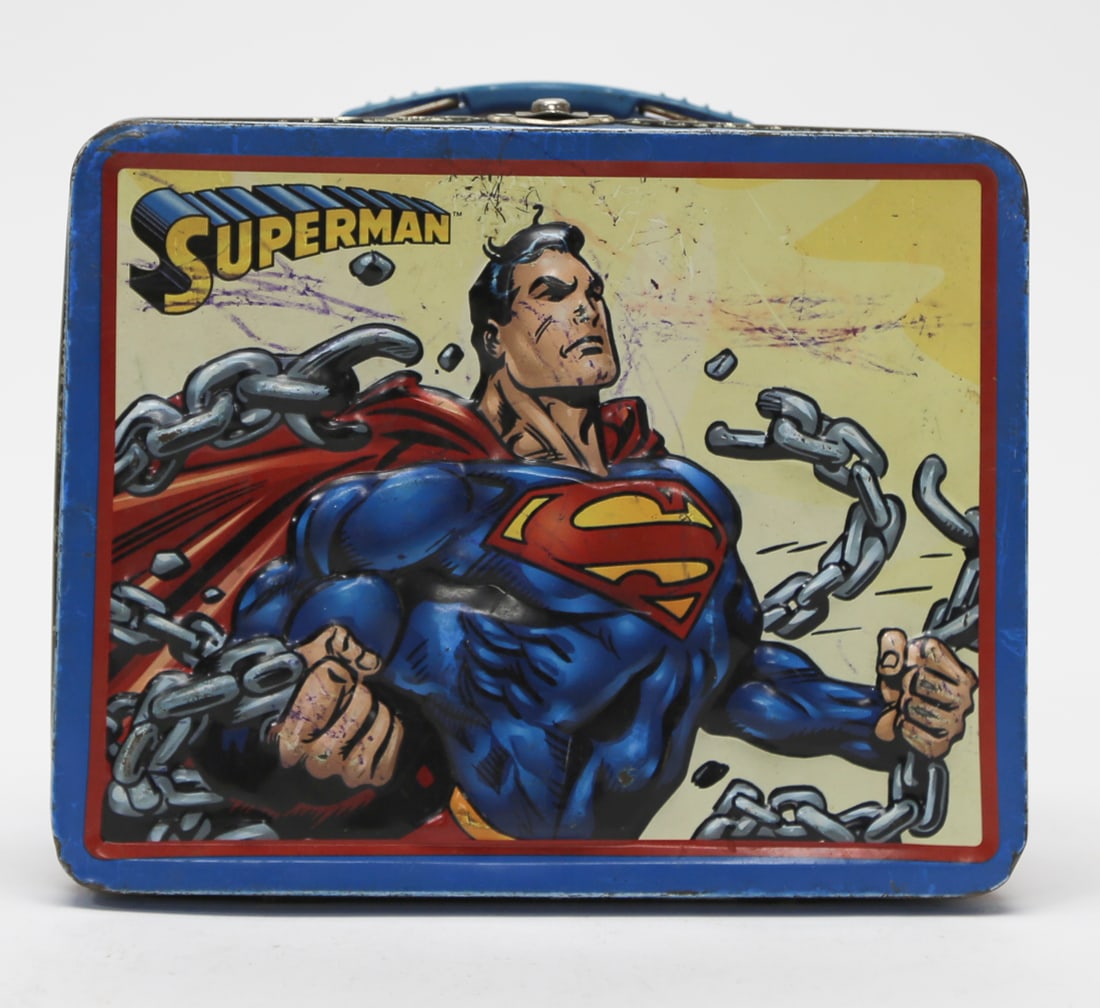 DC Comics Superman Breaking Chains Metal Lunch Box: A modern DC Comics metal lunch box featuring Superman breaking chains against a yellow background. The blue and red box retains its blue plastic carrying handle and metal latch, with Superman emblems 
