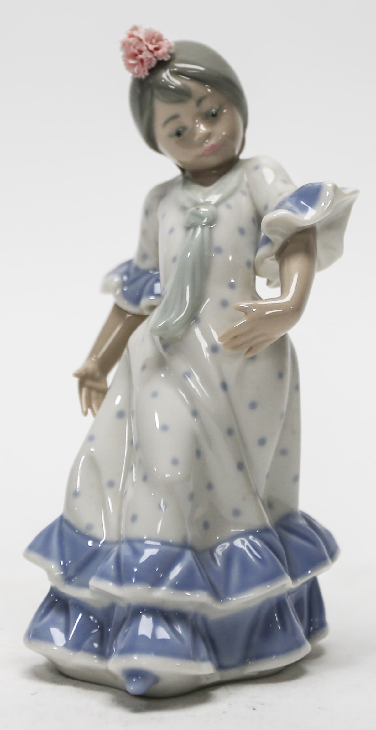 Nao by Lladro Spanish Flamenco Dancer Porcelain Figurine: Glazed porcelain figurine by Nao, a Lladro company, depicting a young Spanish flamenco dancer posed with one hand at her waist and the other extended beside her flowing skirt. She wears a white dress 