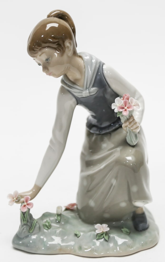 Lladro Picking Flowers Porcelain Figurine No. 1287: Retired Lladro glazed porcelain figurine titled Picking Flowers, model No. 1287. The composition depicts a young woman kneeling in a garden while gathering delicate blossoms. She holds a bouquet of in