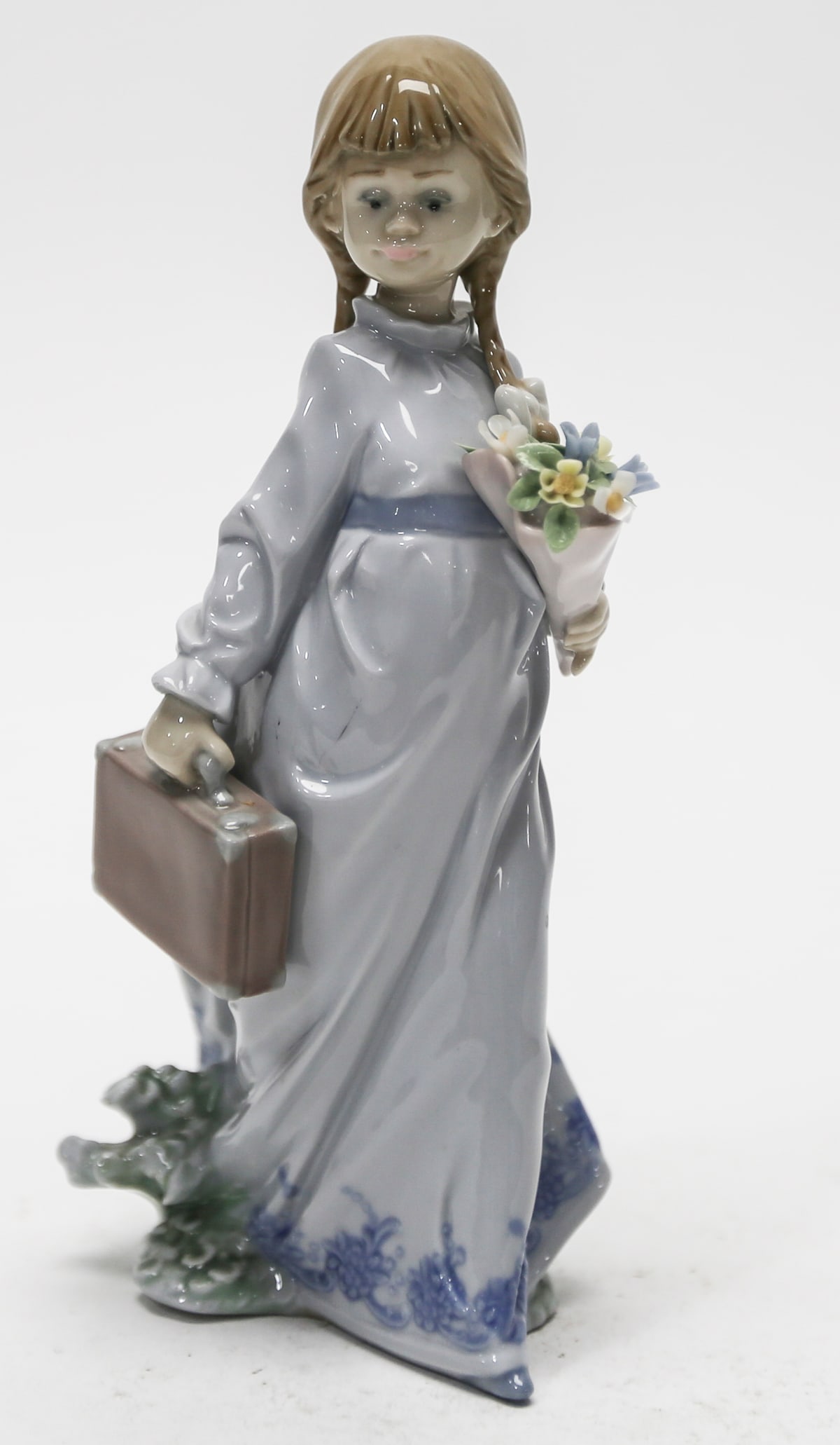 Lladro School Days Porcelain Figurine No. 7604: Retired Lladro glazed porcelain figurine titled School Days, model No. 7604. The piece depicts a young schoolgirl with braided hair and white bows, dressed in a flowing pale blue-gray gown with a dark