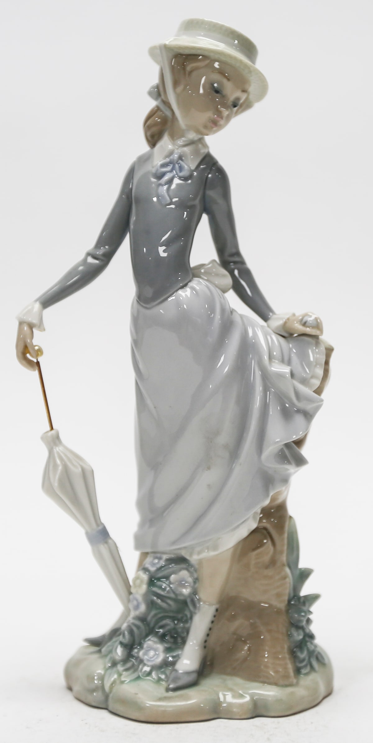 Lladro Young Lady in Trouble Porcelain Figurine Number 4912: Retired Spanish glazed porcelain figurine titled Young Lady in Trouble, designed by Salvador Debon for Lladro. Depicts an elegantly dressed young woman holding a closed umbrella beside a tree stump, f