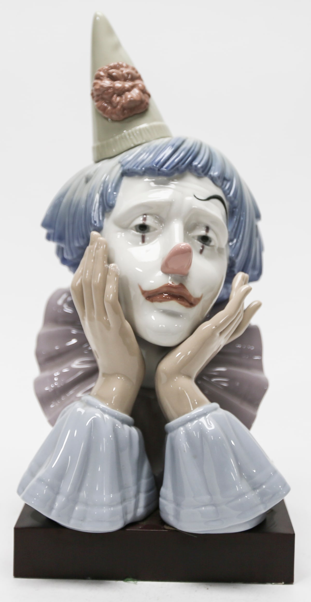 Lladro Pensive Clown Porcelain Bust Number 5130: Retired Spanish glazed porcelain sculpture titled Pensive Clown designed by Jose Puche for Lladro. The expressive composition depicts a melancholy clown resting his face between both hands with a down