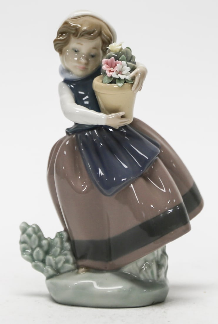 Lladro Spring Is Here Porcelain Figurine Number 5223: Retired Spanish glazed porcelain figurine titled Spring Is Here. The charming composition depicts a young girl wearing a traditional bonnet blue apron and full brown skirt while carefully embracing a 