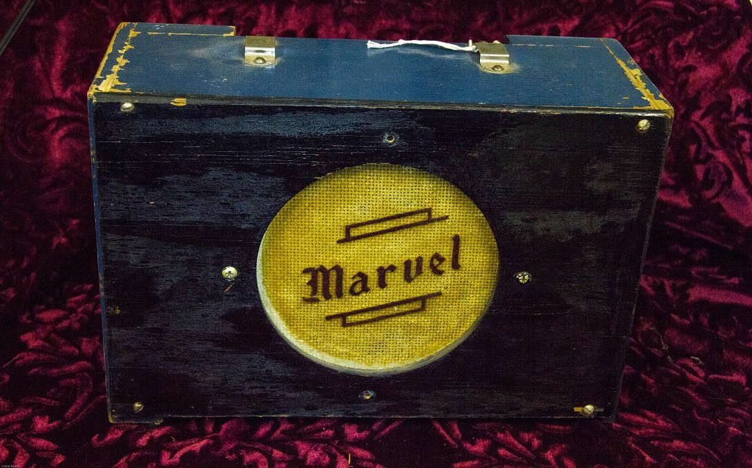 EARLY MARVEL SMALL GUITAR AMPLIFIER IN ORIGINAL BLUE: EARLY MARVEL SMALL GUITAR AMPLIFIER IN ORIGINAL BLUE PAINT, PAINT HAS WEAR AS PICTURED. MEASURES 11 1/2" ACROSS, 8" HIGH AND 5 1/2" DEEP. FRONT PANEL HAS BLACK PAINT. STRAP HANDLE IS BROKEN AT ONE END
