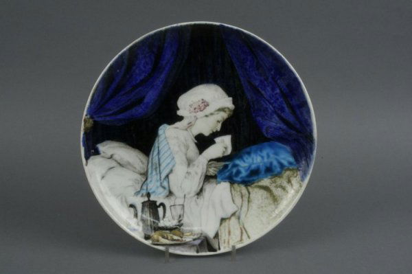 A Theodore Deck wall plate, 11.5in.: A Theodore Deck wall plate, painted with a girl drinking coffee in bed, impressed and painted marks and date 1867, 11.5in.