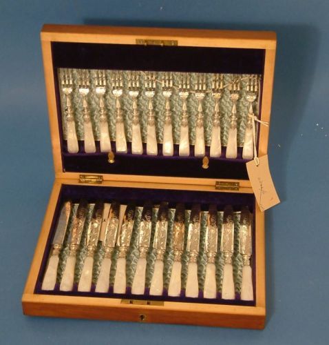 Cased set of 12 plated dessert knives & forks: A cased set of twelve pairs of late Victorian / Edwardian silver plated dessert knives & forks, with engraved scroll decoration and mother of pearl handles, mahogany case with pale blue ruched fabric