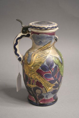 A German pottery lidded jug, 9ins: A German pottery lidded jug, with English arts & crafts painted decoration of birds amidst foliage, monogrammed below possibly for John Pearson, 9ins