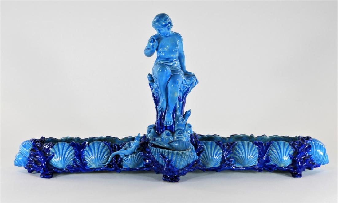 Phillips & Pierce Majolica Sea Nymph Centerpiece: ENGLAND, LATE 19-EARLY 20TH CENTURY An English turquoise majolica centerpiece of a sea nymph retailed by W. P. & G. Phillips & Pierce of London. A nude sea nymph is seen seated on stump startled by a 