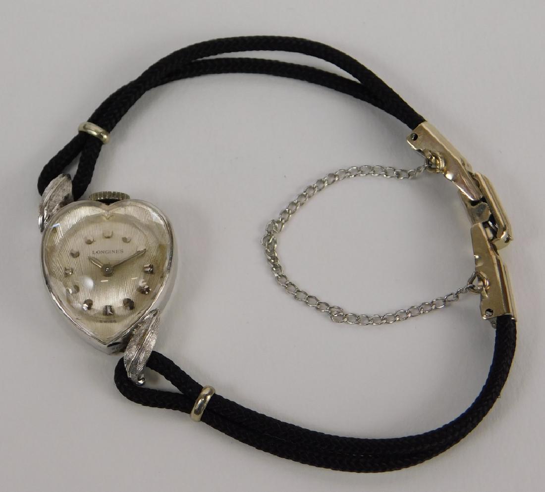 Longines Lady's 14K White Gold Heart Shape Watch: Switzerland,Circa 1960 14K white gold heart shaped bezel on fabric cord band. Weight as seen 19.6 grams. 14K gold, glass, fabric,7" long, From the estate of an Attleboro, Massachusetts lady.