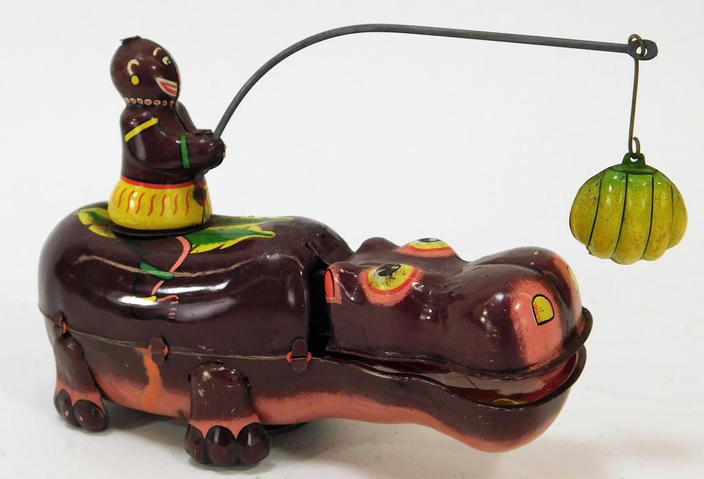 TPS Japan Tin Litho Mechanical Happy Hippo: Japan,Circa 1950 Toy with light surface scratching and wear to paint and does not wind up. O Tin litho,4" t x 2" w x 5 1/2" d, Marked "T.P.S. Made in Japan" underneath hippo's jaw. From the collection