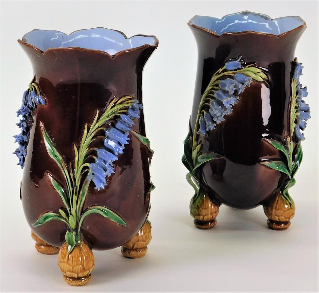 PR Minton Majolica Aesthetic Tripod Flower Vases: England,Early 20th Century Two squat vases with scalloped edges, applied bluebells, and three shapely feet against a burgundy ground. Pottery,7" x 4 1/4" dia., Each marked "Minton" on bottom. From the