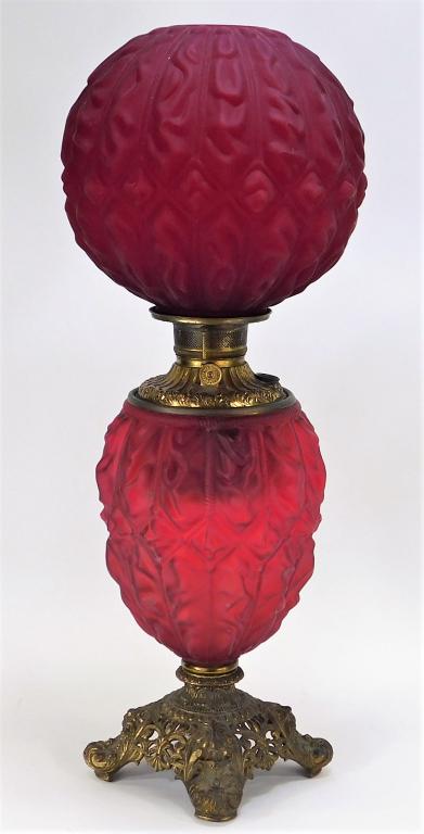Gone With the Wind Cranberry Satin Glass Oil Lamp: United States,Late 19th-Early 20th Century Molded glass shade and body with ornate burner supported by a four footed acanthus leaf and fleur-de-lis decorated base. Glass, brass,Overall 27 3/4" x 9" di