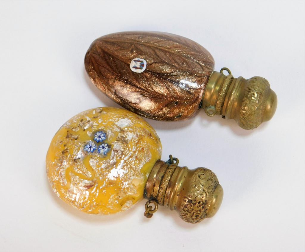 2PC Victorian Glass Scent Bottle Vinaigrettes: Europe 19th Century Includes a round silver and yellow glass bottle with three blue millefiori flowers to one side and a face on the other, and one oblong bottle with sparkling brown feather design an
