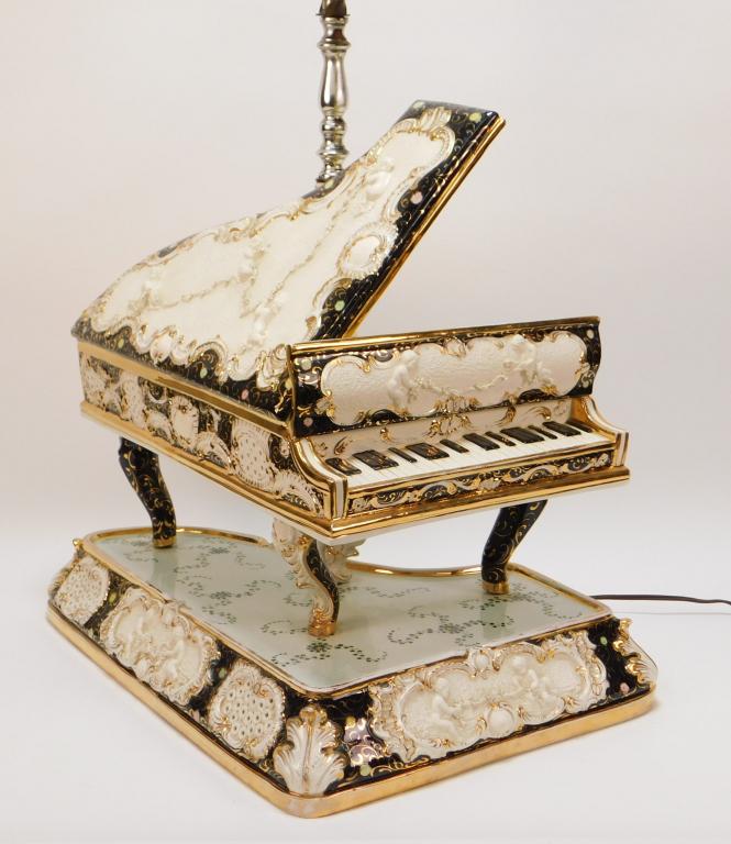 Italian Capodimonte Gilded Piano Lamp: Italy 20th Century Large piano shaped column decorated with cherubs and flower garlands throughout. Lamp 32 1/4" t x 12 7/8" w x 17 7/8" d,Lampshade 18 3/4" x 19 5/8" dia.,Porcelain, metal Marked "Ita