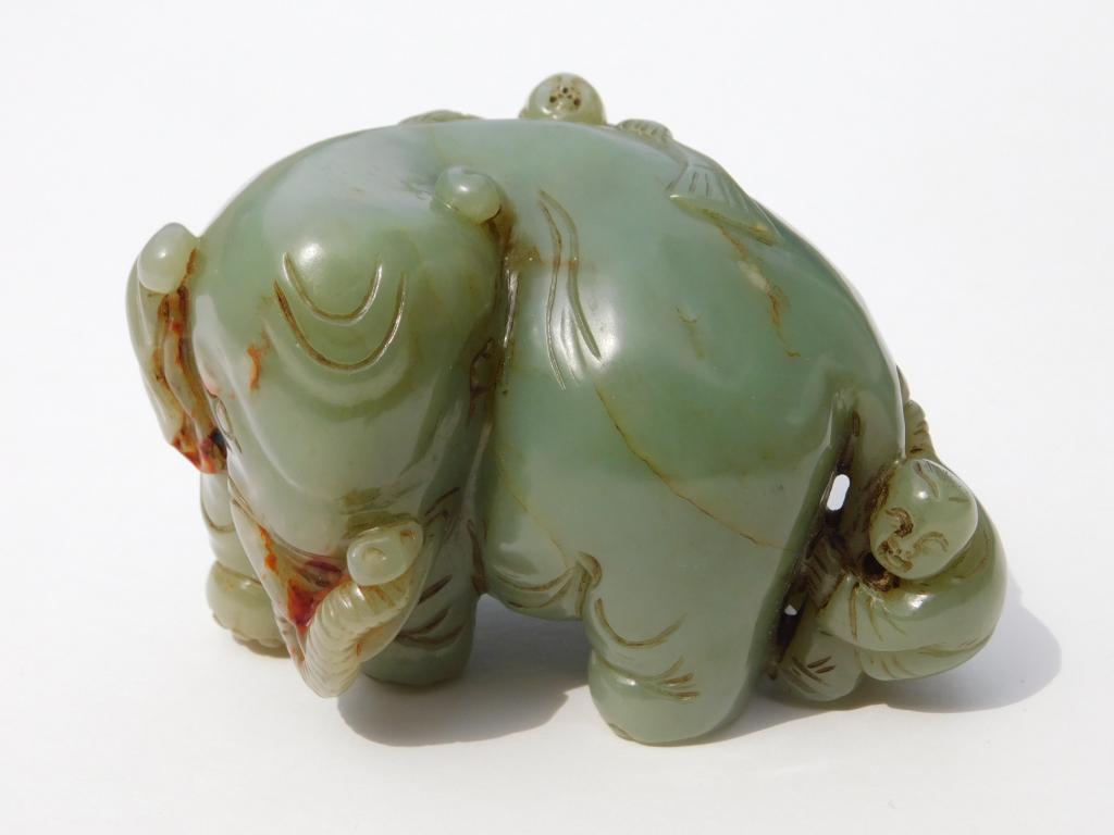 Chinese Qing Dynasty Carved Jade Elephant: China,Qing Dynasty Depicts an elephant with head turned to face behind it with two children clinging to its back and tail, carved from celadon jade with russet inclusions. Jade,2 5/8" t x 3 7/8" w x 2