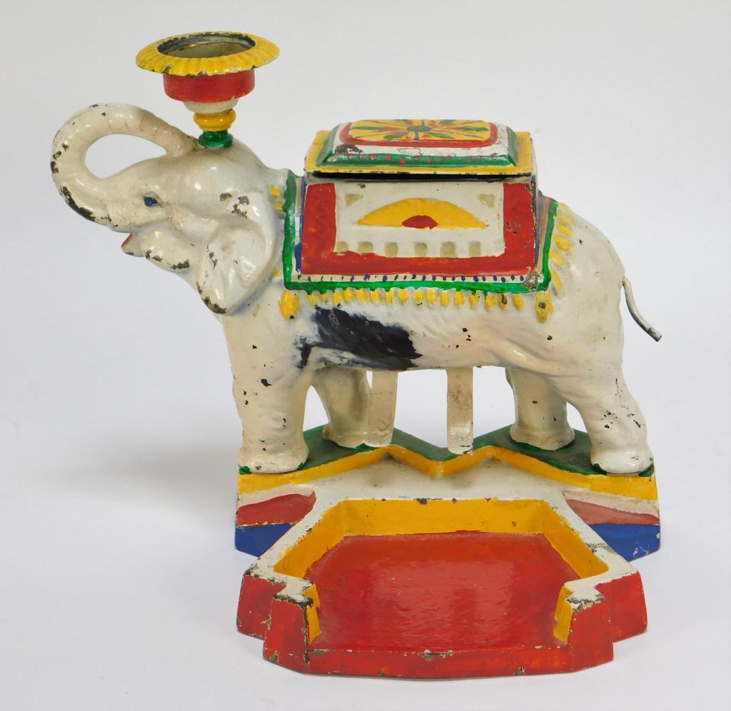Polychrome Cast Iron Elephant Cigarette Dispenser: United States,Early 20th Century Figural elephant with upward turned trunk, box opens to reveal cigarette container and turn tail to individually dispense,7 1/2" t x 9" w x 6 1/4" d. From the collecti