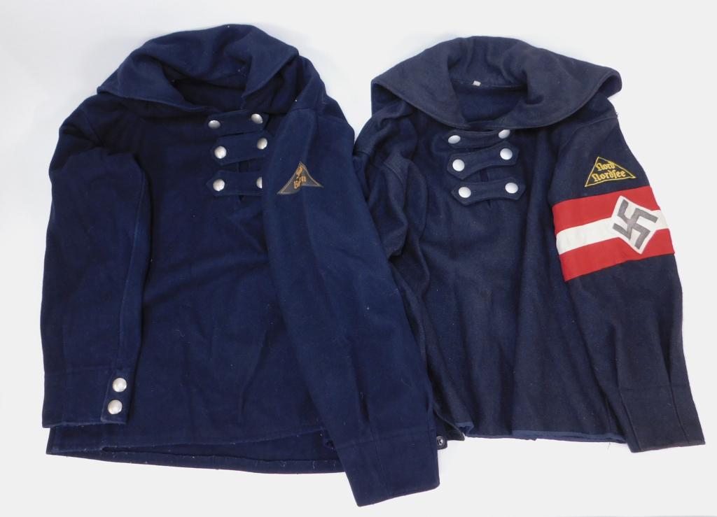 Two WWII German DJ Winter Blouses: Germany C. 1926-45 A black woolen pull over winter blouse with a cape and three neck closure straps, pebbled buttons, patch on the left sleeve marked "nord/norfee," with an HJ armband, and a black woo