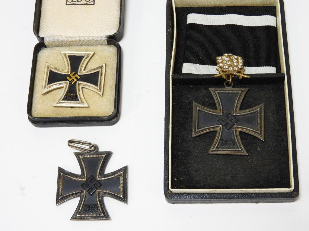 Three WWII German Iron Crosses: Germany C. 1939-45 A cased iron cross, marked on the inside of the lid "LDO," a black enameled silver iron cross marked "330" on the upper back left, and a cased iron cross with a paste oak leaf and r