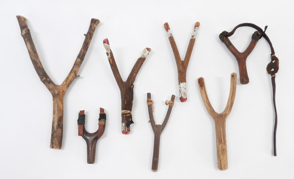 7PC Vintage Wood Slingshots: United States Early 20th Century Includes seven wood slingshot with some retaining original paint, leather straps, and rubber. Wood,Smallest 4 3/4" x 2 1/2".Largest 13" x 8 1/2" From the collection of