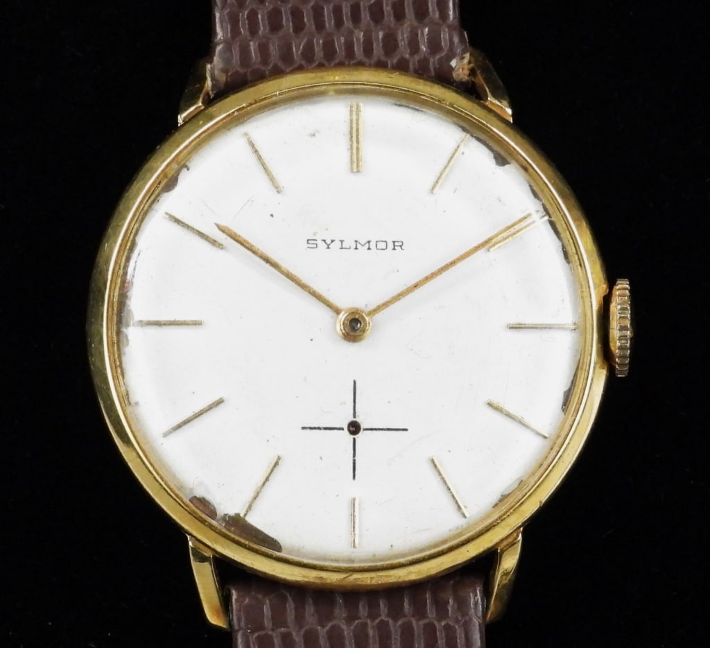18K Gold Sylmor Wristwatch: White watch face with line chapter marks housed in an 18K gold yellow case with brown leather strap. 18K gold, leather,Case diameter 33mm.Length 9" Face marked "Sylmor" From the collection of a Bristo