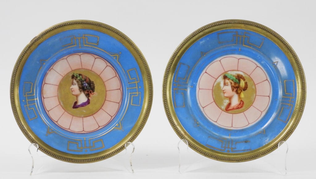 PR French Sevres Porcelain Cameo Plates: France Late 19th- Early 20th Century Pair of neoclassical cameo centers depicting side profiles of women with braided hair and laurel wreaths over gild surrounded by blue and brass mounted rims. Porce