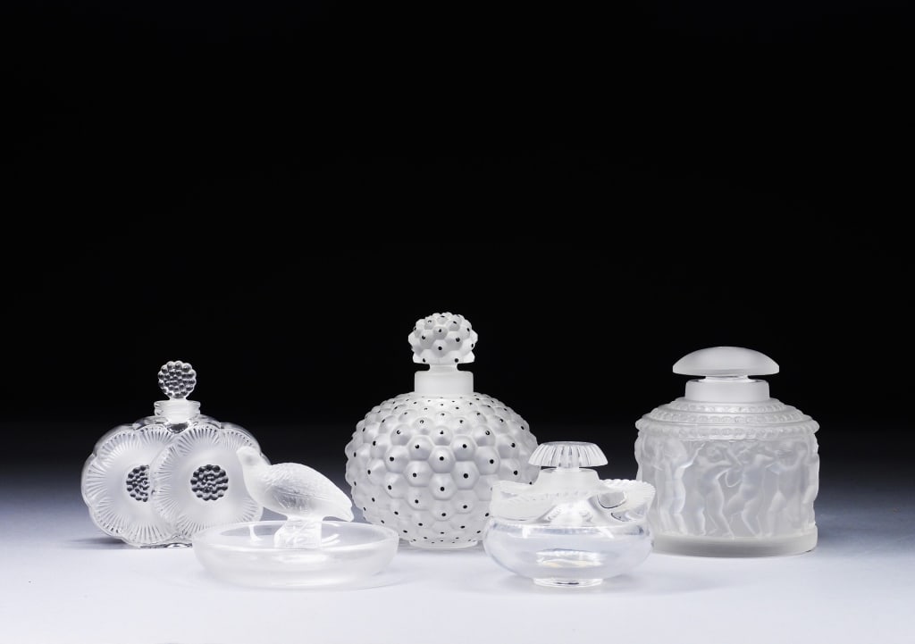 5PC Lalique Art Glass Perfume Dresser Bottles: France,20th Century Includes a Cactus perfume bottle, a Baptiste perfume bottle, a quail ring dish, a Deux Fleurs perfume bottle, and a Les Enfants perfume bottle. Lalique was founded in 1888 by renow