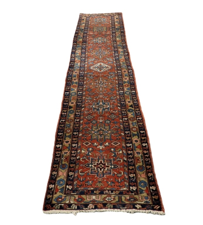 Heriz Geometric Carpet Rug Runner: Middle East,20th Century Blue, navy blue, red, tan, pink, and ivory repeating geometric pattern over red field surrounded by geometric floral boarders. Wool,Approx. 13' x 3'. From the collection of a 