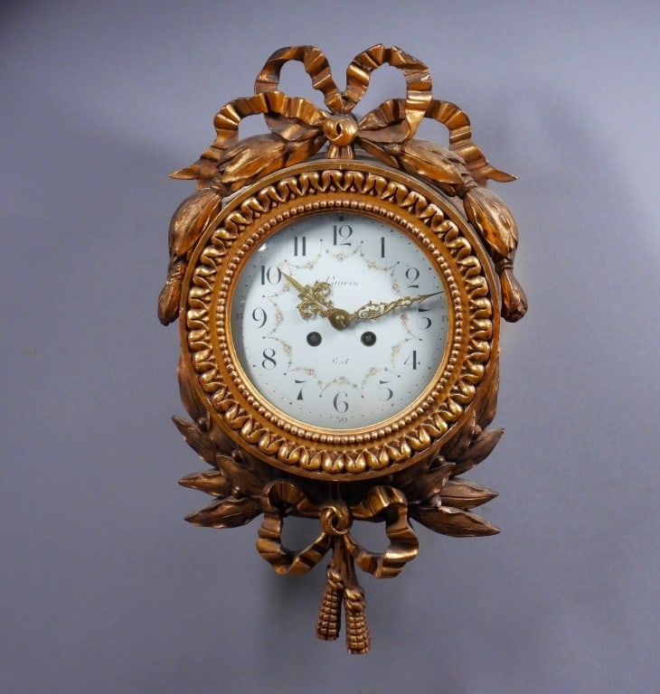 Samuel Marti French Louis XV Style Cartel Clock: France,19th Century White enamel face clock with black Arabic numeral numbering and botanical swags housed in a carved wood gilt case comprised of ribbon elements. Samuel Marti was a renowned clockmak