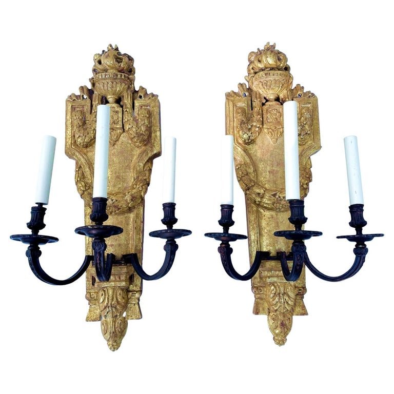 Pair of Italian Gilded Wood Sconces: A pair of Italian 3-light carved and gilded sconces with bronzed metal arms each having a faux candle light. The sconces are large in size and very substantial. Measurements: 31 inches high x 14.50 in
