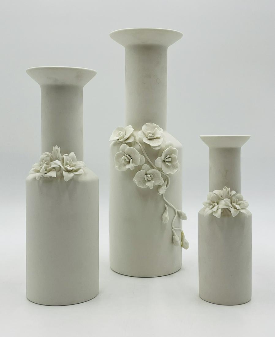 Set of Graduated Porcelain Vases: A set of three graduated white porcelain vases detailed with refined hand sculpted and mounted flowers. Measurements: From big to small 14 inches high x 4.50 inches in diameter 11.50 inches high x 3.7