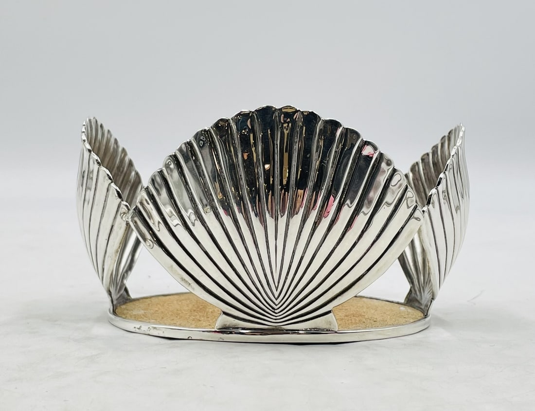 Emilia Castillo Silver-Plated Shell Motif Wine Bottle Coaster, Signed: Elegant and sculptural silver-plated wine bottle holder by Emilia Castillo, featuring four stylized scallop shell panels arranged symmetrically around a circular base. The interior is lined with natur