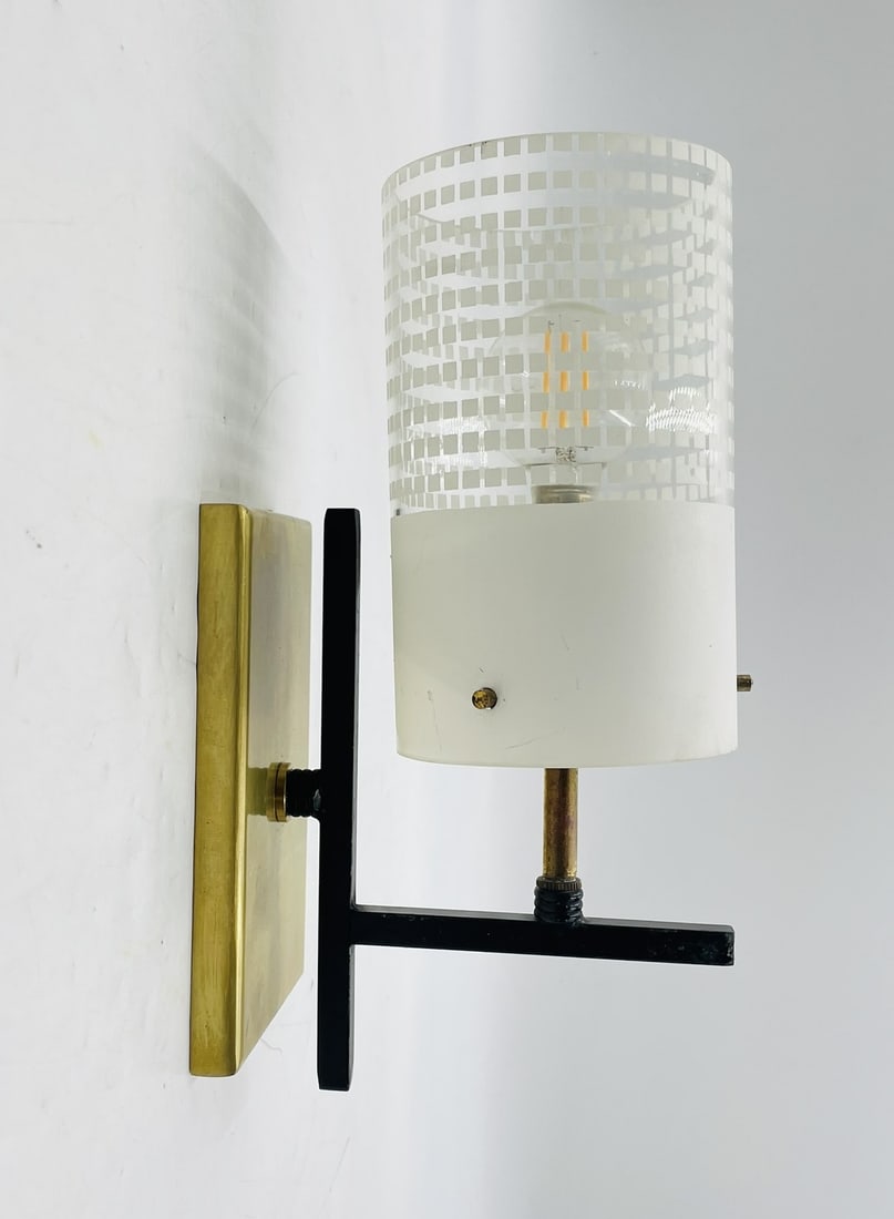 Mid-Century Modern Brass and Glass Wall Sconce in the Manner of Stilnovo: A striking Mid-Century Modern wall sconce crafted in the manner of Stilnovo, featuring a brushed brass backplate, black enamel arm, and a distinctive cylindrical glass shade with an etched geometric p