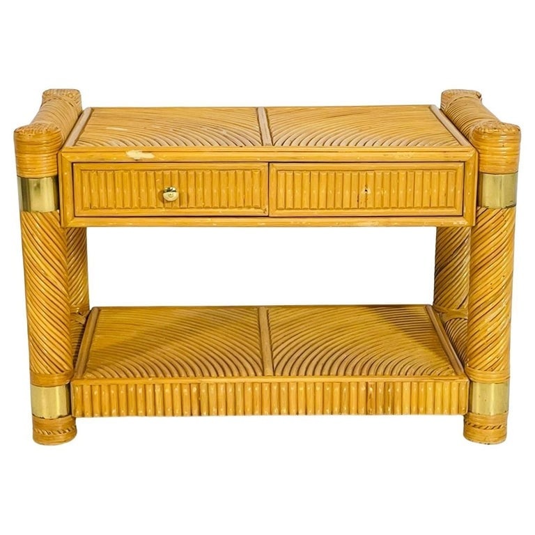 Brass and Pencil Reed Console Table After Karl Springer: A charming vintage console table crafted from bent rattan with a lacquered honey-toned finish and stylish brass banding accents. This piece features beautifully curved reedwork on the tabletop and low