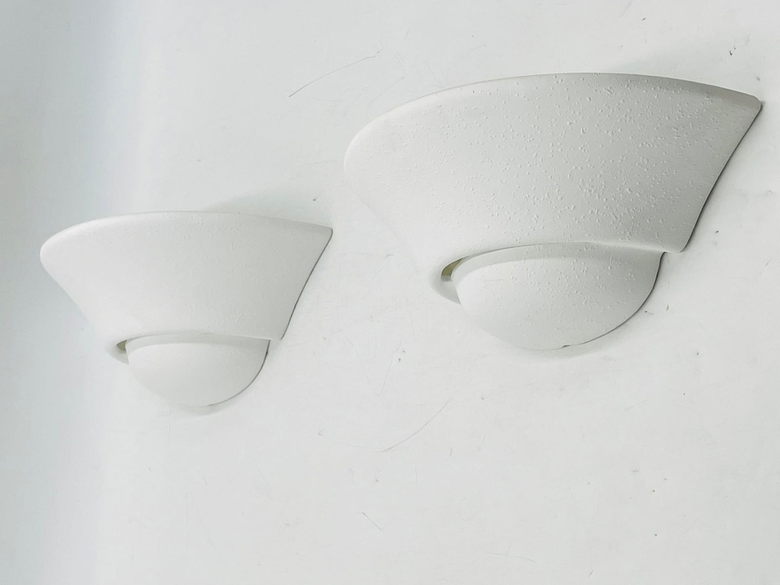 Pair of Modern White Ceramic Wall Sconces: Sleek and minimal pair of white ceramic wall sconces with a textured matte finish. These contemporary light fixtures feature a flared half-dome shape and upward-facing design for a soft, ambient glow.