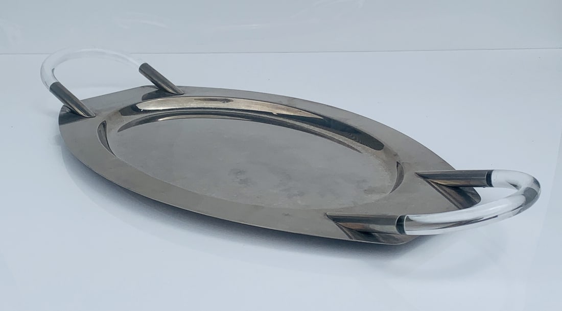 Mid-Century Modern Oval Serving Tray with Lucite Handles: A striking mid-century modern oval serving tray featuring sleek polished metal construction paired with clear Lucite handles for a contemporary flair. The streamlined silhouette and minimalist aesthet