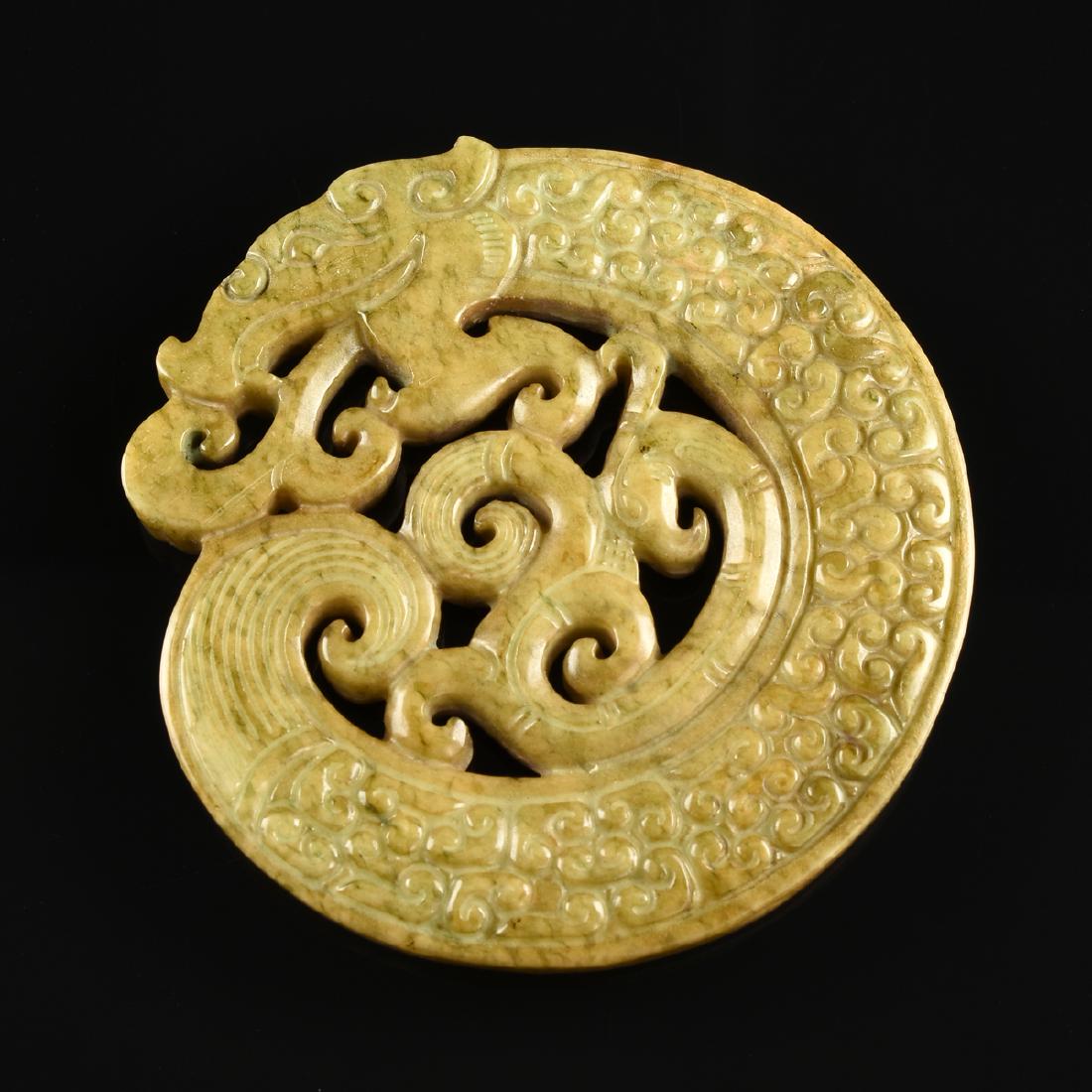 A CHINESE MOTTLED GREEN JADE PENDANT, IN THE ZHAO: A CHINESE MOTTLED GREEN JADE PENDANT, IN THE ZHAO DYNSTASTY (1027-771 BC) STYLE, pierced carved, at center, a recumbent phoenix, encircled by a dragon with stylized archaic form scales, breathing clou