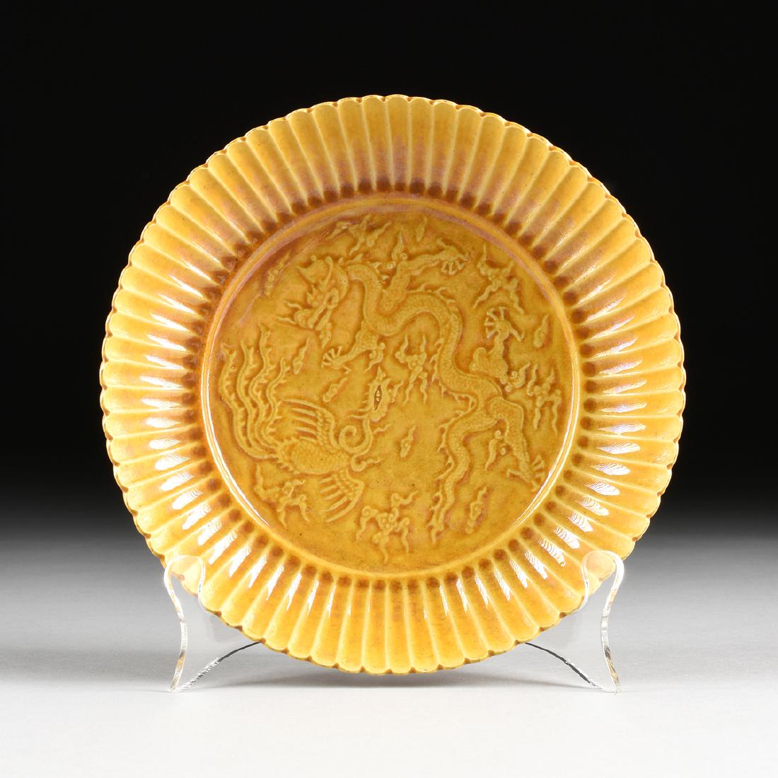 A CHINESE YELLOW GROUND CARVED PORCELAIN DISH,: A CHINESE YELLOW GROUND CARVED PORCELAIN DISH, with mustard yellow fluted rim, centering carved dragon and phoenix decoration, six character Hongzhi (1488-1505) reign mark within double black circle,