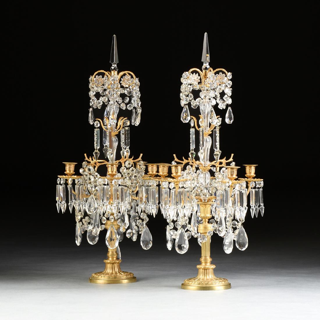 A PAIR OF LOUIS XVI STYLE GILT METAL AND CUT CRYSTAL: A PAIR OF LOUIS XVI STYLE GILT METAL AND CUT CRYSTAL FIVE LIGHT GIRANDOLES, FRENCH, LATE 19TH CENTURY, each in the Baccarat taste, centering cut spear finials over crooked scrolls sandwiched by cut ro