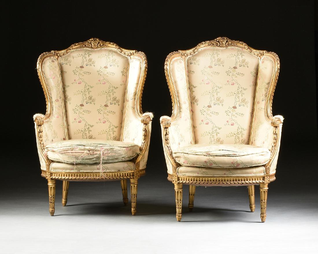 A PAIR OF LOUIS XVI STYLE GILTWOOD BERGÈRE À OREILLES,: A PAIR OF LOUIS XVI STYLE GILTWOOD BERGÈRE À OREILLES, IN THE ITALIAN TASTE, EARLY/MID 20TH CENTURY, the arched crest rail centering a flowering basket, issuing bell flower chains over ribbon twist 