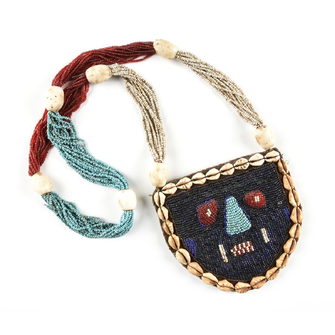 A WEST AFRICAN MILK GLASS, SEED BEAD AND COWRIE SHELL: A WEST AFRICAN MILK GLASS, SEED BEAD AND COWRIE SHELL MASK NECKLACE, large ovoid milk glass beads intersperse red, white and blue glass beads, centering a mask with scarred cheeks, length: 21".