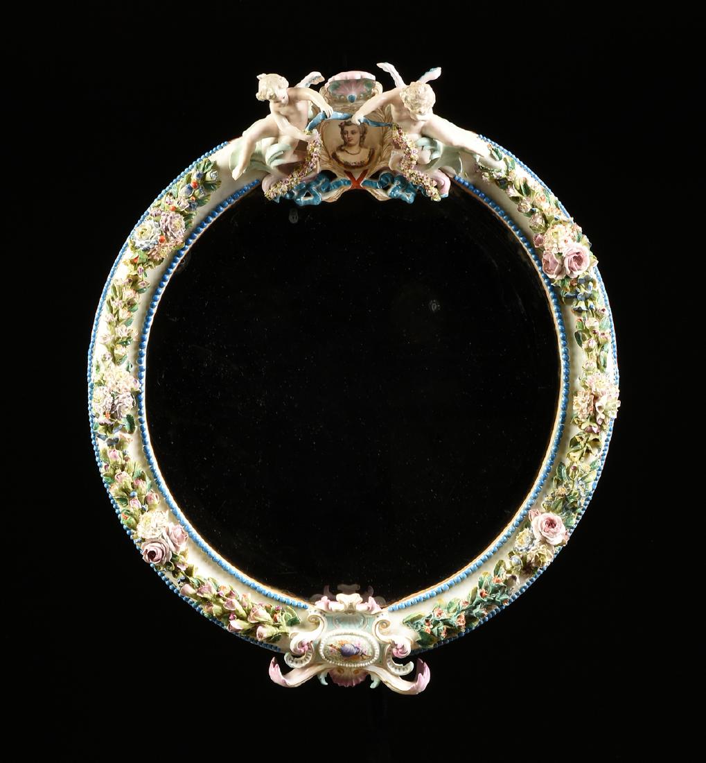 AN ANTIQUE DRESDEN POLYCHROME PAINTED AND FLORAL: AN ANTIQUE DRESDEN POLYCHROME PAINTED AND FLORAL ENCRUSTED TOILETTE MIRROR, LATE 19TH/EARLY 20TH CENTURY, the circular beveled mirror set within a conforming frame surmounted by an oval cartouche cent
