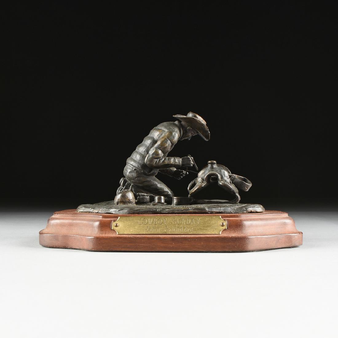 JOHN SAUNDERS (AMERICAN 20TH CENTURY) A BRONZE: JOHN SAUNDERS (AMERICAN 20TH CENTURY) A BRONZE SCULPTURE, "Cowboy Sunday," a patinated cast bronze cowboy kneeling alongside his tools as he repairs his saddle, on a stylized groundwork bronze base in