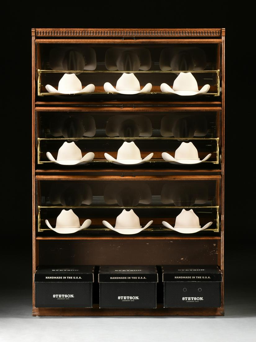 A MERCHANT'S COWBOY HAT CURVED GLASS OAK DISPLAY CASE,: A MERCHANT'S COWBOY HAT CURVED GLASS OAK DISPLAY CASE, AMERICAN, LATE 19TH/EARLY 20TH CENTURY, in the arts and crafts taste and echoing barrister bookcase forms, the crest with applied repeating moldi
