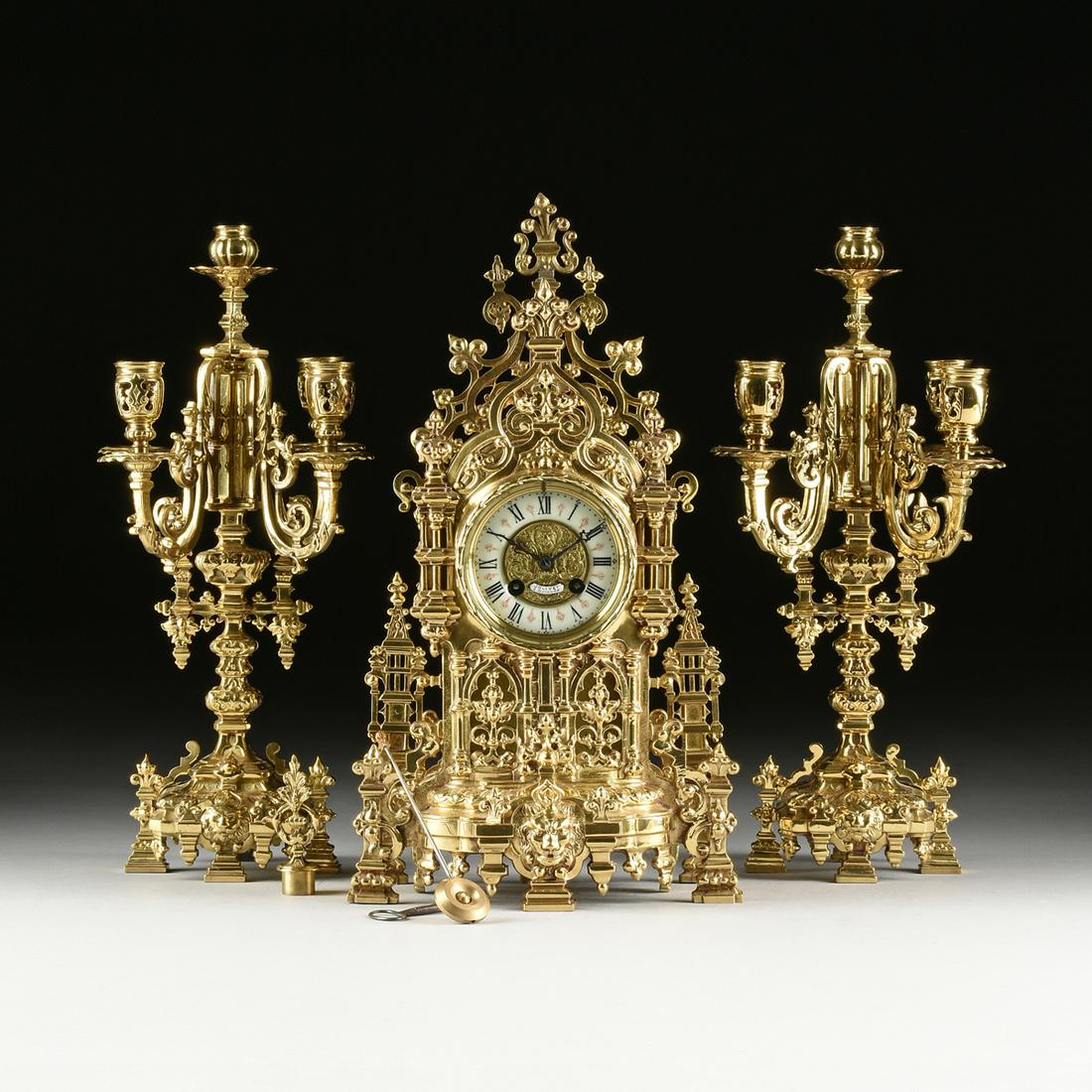 A FRENCH JAPY FRERES WORKS GOTHIC REVIVAL GILT BRASS: A FRENCH JAPY FRERES WORKS GOTHIC REVIVAL GILT BRASS THREE PIECE GARNITURE, NAPOLEON III (1852-1873), the pointed arches within a profusion of pierced foliate scrolls, the clock face with repousse cen