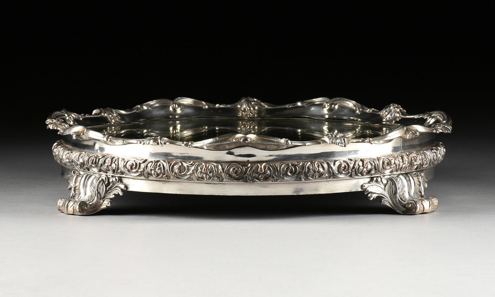 A ROCOCO REVIVAL SILVERPLATE MIRRORED PLATEAU, MID/LATE: A ROCOCO REVIVAL SILVERPLATE MIRRORED PLATEAU, MID/LATE 19TH CENTURY, in the Victorian English taste, the scalloped molded edge centering a mirrored plate, the edge with relief flower bouquets and scr